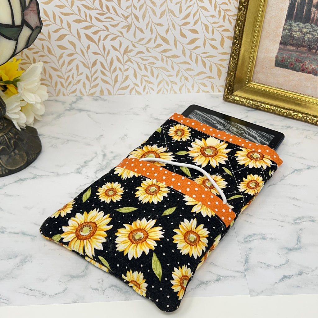 this picture shows a quilted fabric eReader case. The fabric has colorful yellow daisy floral pattern on a black background. It has coordinating orange with white dots fabric as a trim for the pocket and top of case.