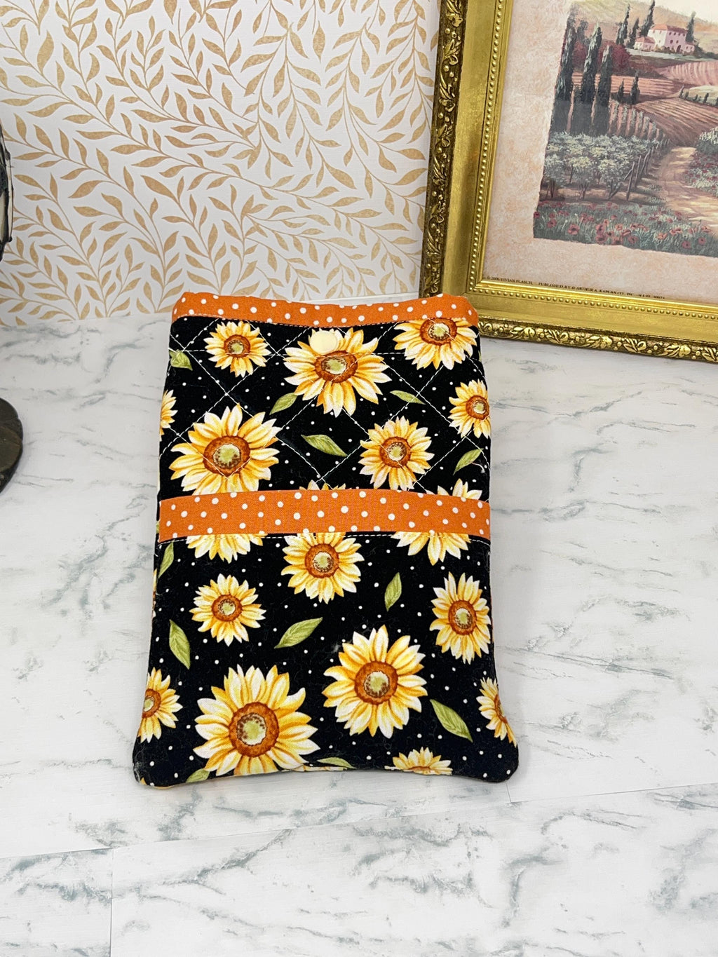 this picture shows a quilted fabric eReader case. The fabric has colorful yellow daisy floral pattern on a black background. It has coordinating orange with white dots fabric as a trim for the pocket and top of case.