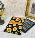 this picture shows a quilted fabric eReader case. The fabric has colorful yellow daisy floral pattern on a black background. It has coordinating orange with white dots fabric as a trim for the pocket and top of case.