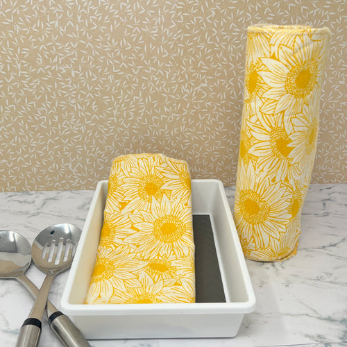 Flannel reusable paper towels. This pictures shows possible display options on Kitchen counter. One group is folded in a basket and the other group rolled on a cylinder. Cotton fabric has a large overlapping  sketch of yellow daisies 