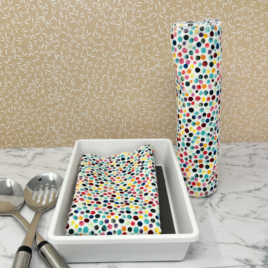 Flannel reusable paper towels. This pictures shows possible display options on Kitchen counter. One group is folded in a basket and the other group rolled on a cylinder. Cotton fabric has a colorful confetti dot pattern on white background. 