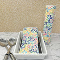 Flannel reusable paper towels. This pictures shows possible display options on Kitchen counter. One group is folded in a basket and the other group rolled on a cylinder. Cotton fabric has a ditzy floral print pattern of tiny colorful flowers on a white background