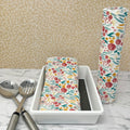 Flannel reusable paper towels  showing possible counter displays with a group folded in a basket and another group rolled onto a cylinder.. Fabric has a floral and greenery  pattern in a painted "style" with red and gold flowers, and greenery on a white background.