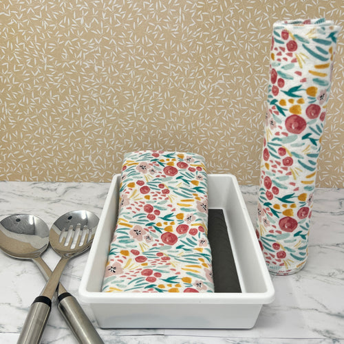 Flannel reusable paper towels  showing possible counter displays with a group folded in a basket and another group rolled onto a cylinder.. Fabric has a floral and greenery  pattern in a painted "style" with red and gold flowers, and greenery on a white background.