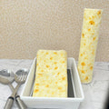 Flannel reusable paper towels. This pictures shows possible display options on Kitchen counter. One group is folded in a basket and the other group rolled on a cylinder. place setting. Cotton fabric has yellow and gold dandelions  on a soft yellow on background