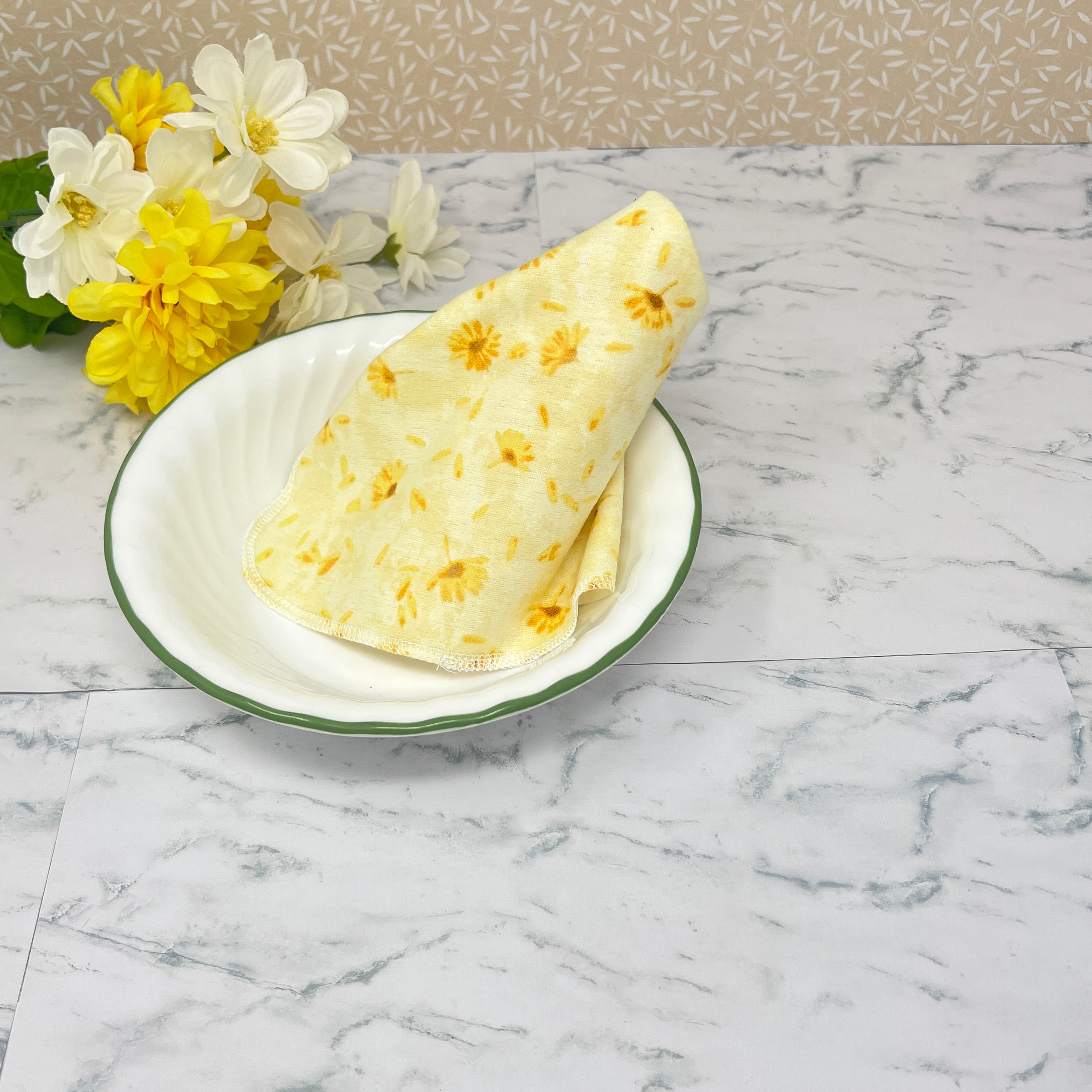 Flannel reusable paper towels. This pictures shows a single towel on a table setting..  Cotton fabric has yellow and gold dandelions  on a soft yellow background