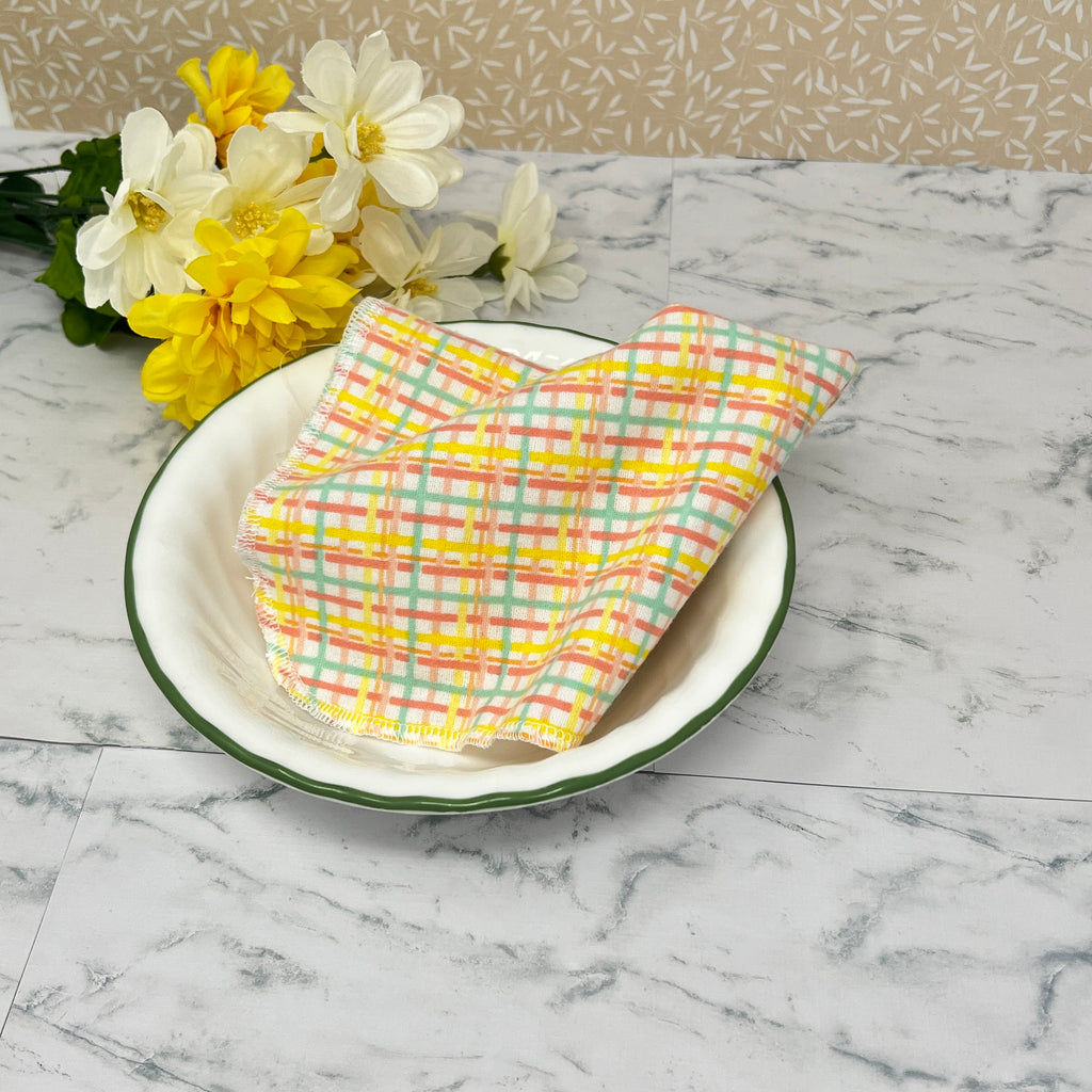 Flannel reusable paper towels. This pictures shows the towel  in a place setting.  Cotton fabric has a yellow, turquoise and light red plaid pattern on a white background