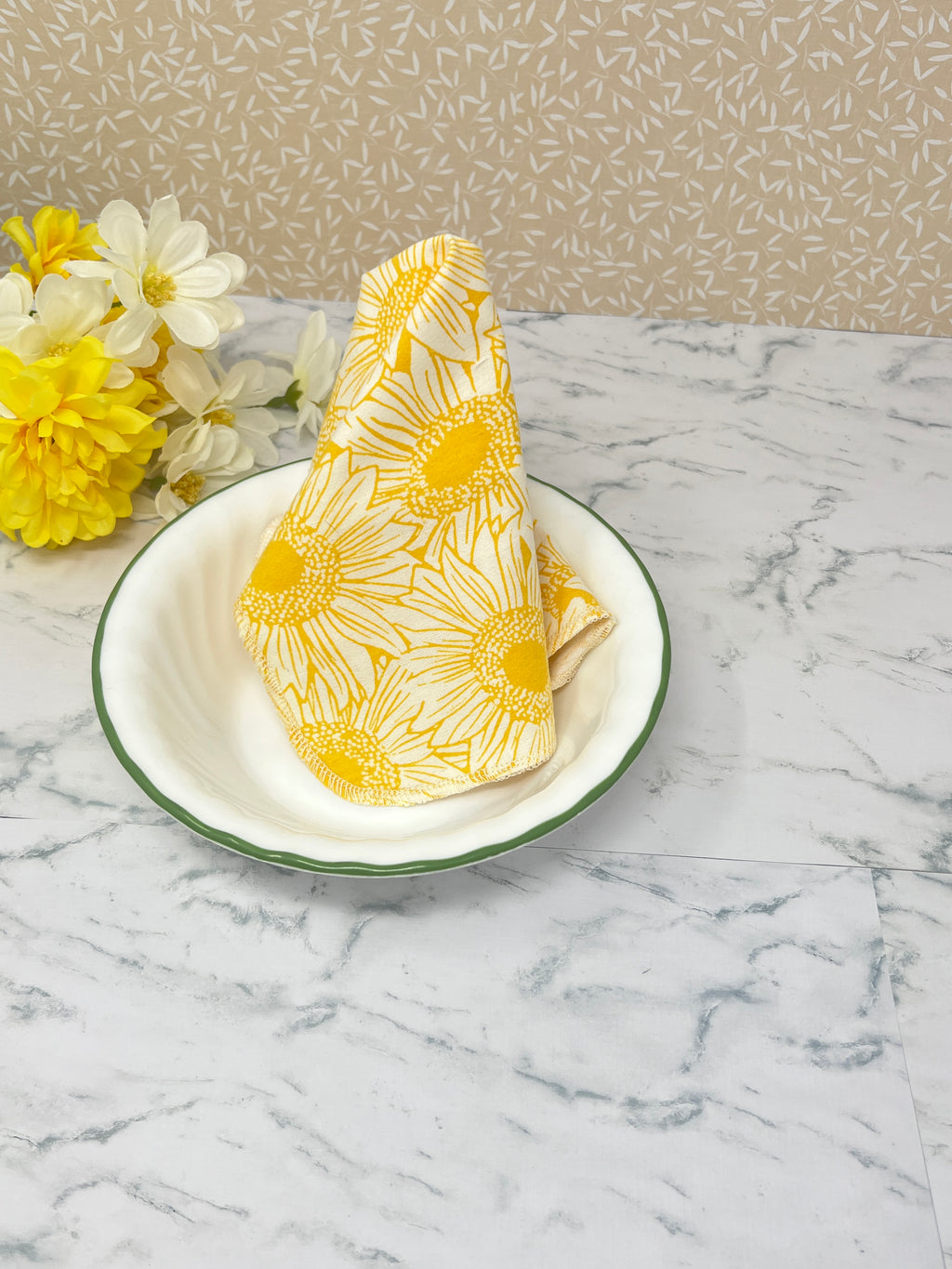 Flannel reusable paper towels. This pictures shows possible use options as a napkin in a table place setting. Cotton fabric has a large overlapping  sketch of yellow daisies 