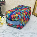 A large quilted makeup bag or cosmetic bag pouch also known as a toiletry bag,  with zipper and handle. Fabric is cotton and has a colorful array of kaleidoscope shapes in varying shades of  blue, red, green and yellow. A coordinating blue handle to match the blue interior lining