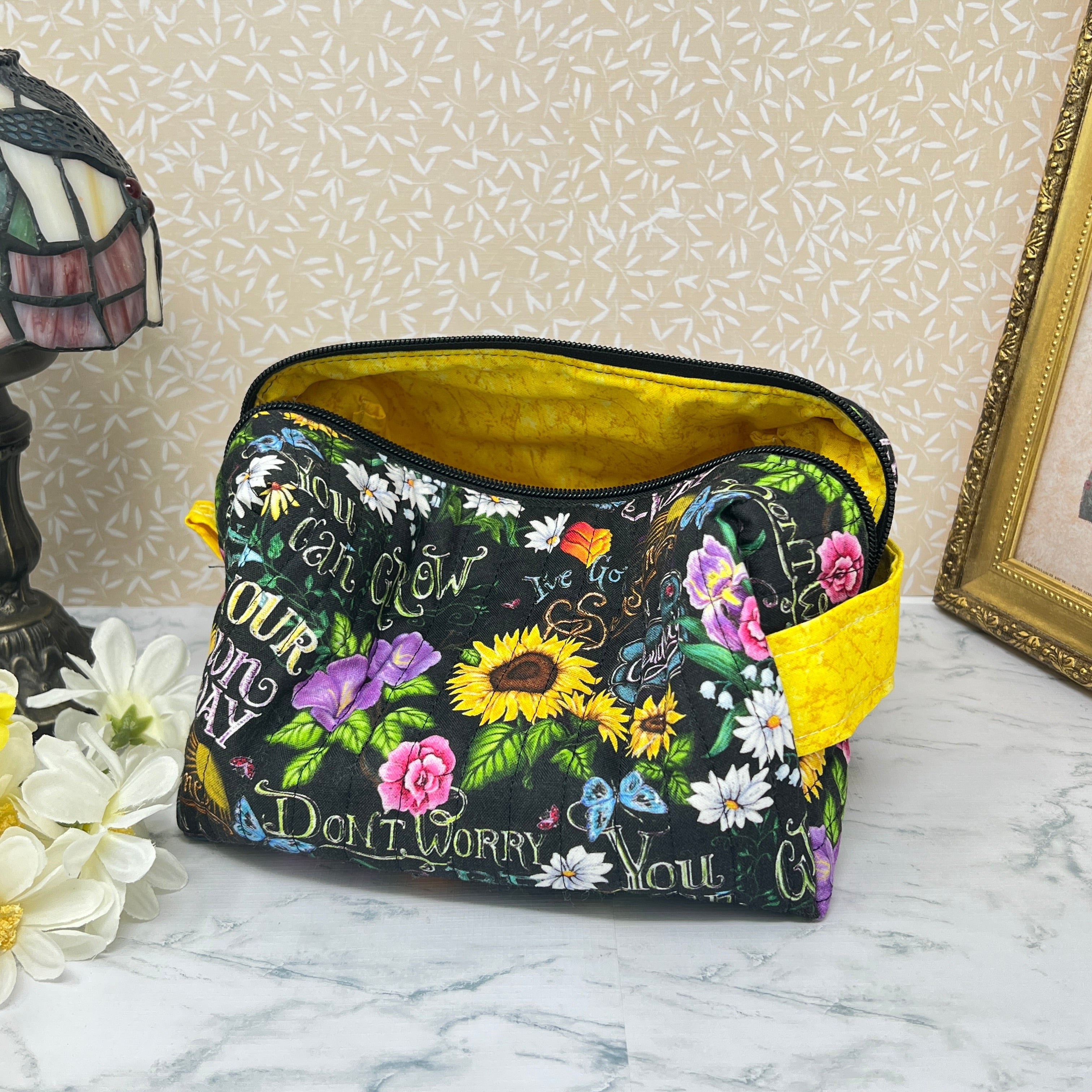A large quilted boxy bag with zipper and handle. Fabric is colorful flowers and positive affirmation text on a black background. Showing Yellow handle and yellow liner