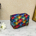 Small quilted makeup bag or cosmetic bag pouch with zipper and handle. Fabric is cotton and has a colorful array of kaleidoscope shapes in varying shades of  blue, red, green and yellow. Blue handle to match lining