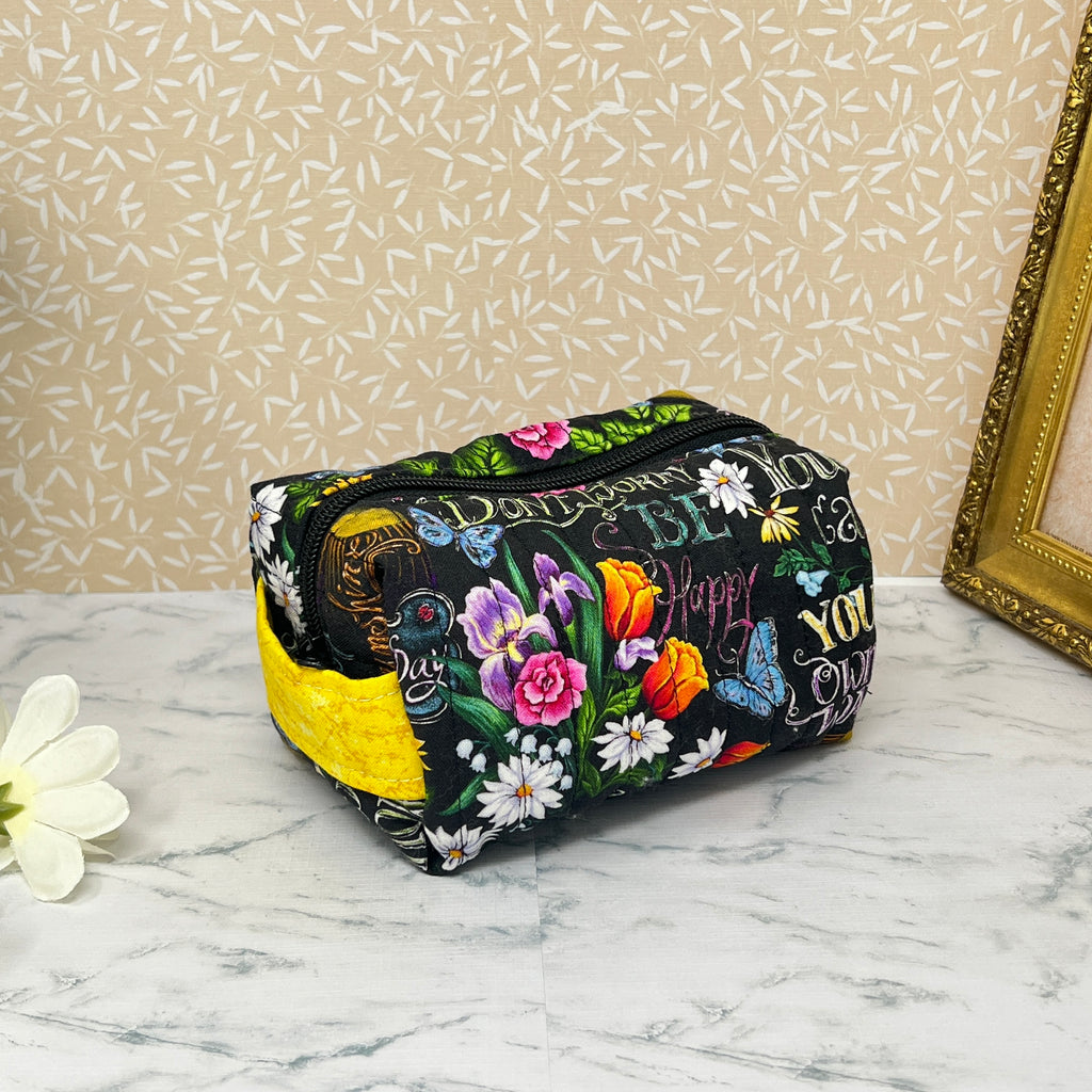 small quilted boxy bag with zipper and handle. Fabric is colorful flowers and positive affirmation text on a black background. Yellow handle and yellow liner